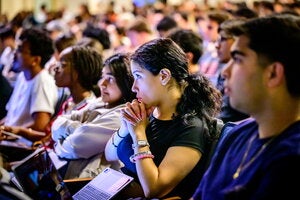 A student sitting in a lecture hall, listening to class.