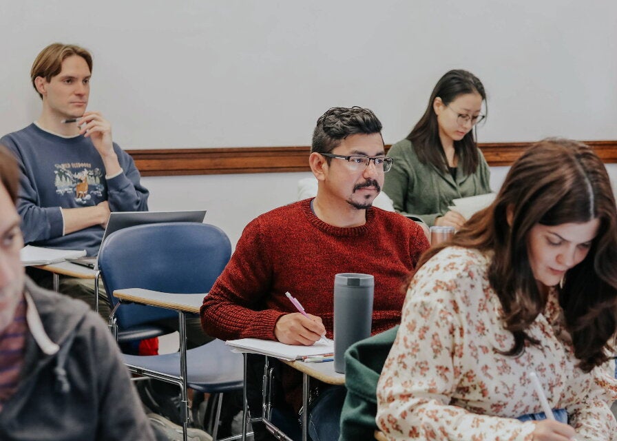 A student sits among peers in a classroom, listening to a lecturer