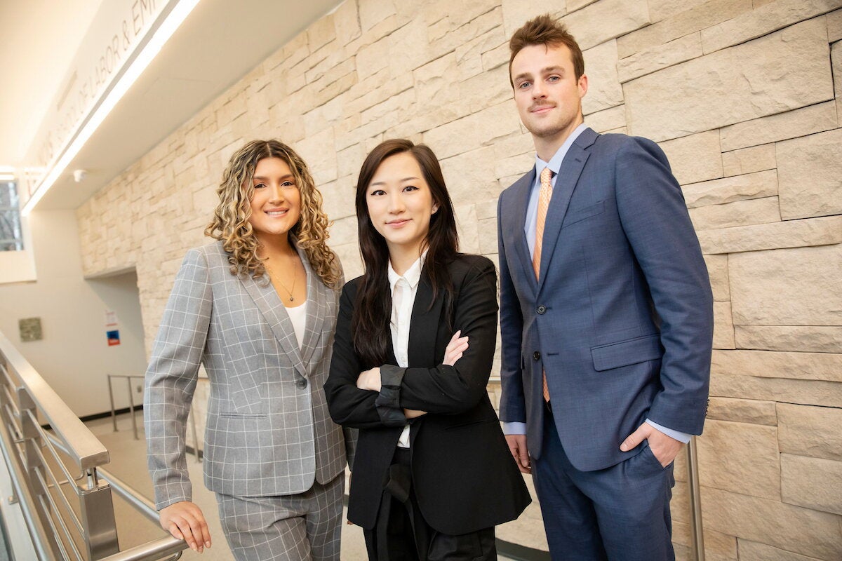 Three students in business professional attire pose together, looking determined.
