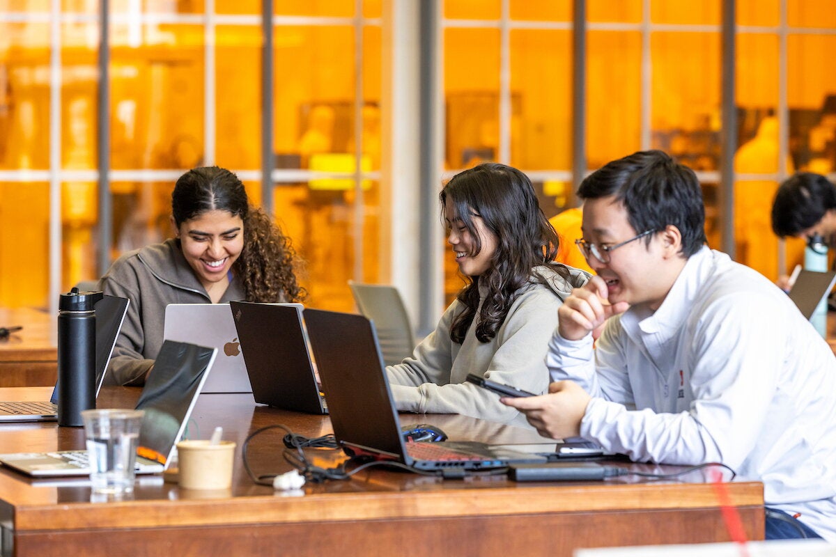 Three students smile as they sit at a table and study together.