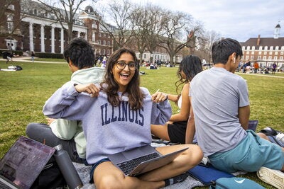 A student points and smiles at her Illini T-Shirt as she hangs out on the Quad with friends.