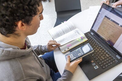 A photo taken over a student's shoulder as they use a calculator to solve a problem.