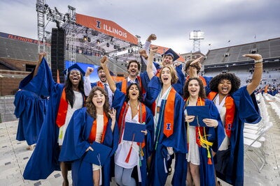 A group of students cheer in their caps and gowns as they celebrate graduation at Gies Memorial Stadium.
