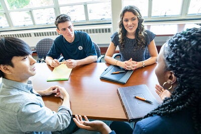 Four students discuss and collaborate while gathered around a table.