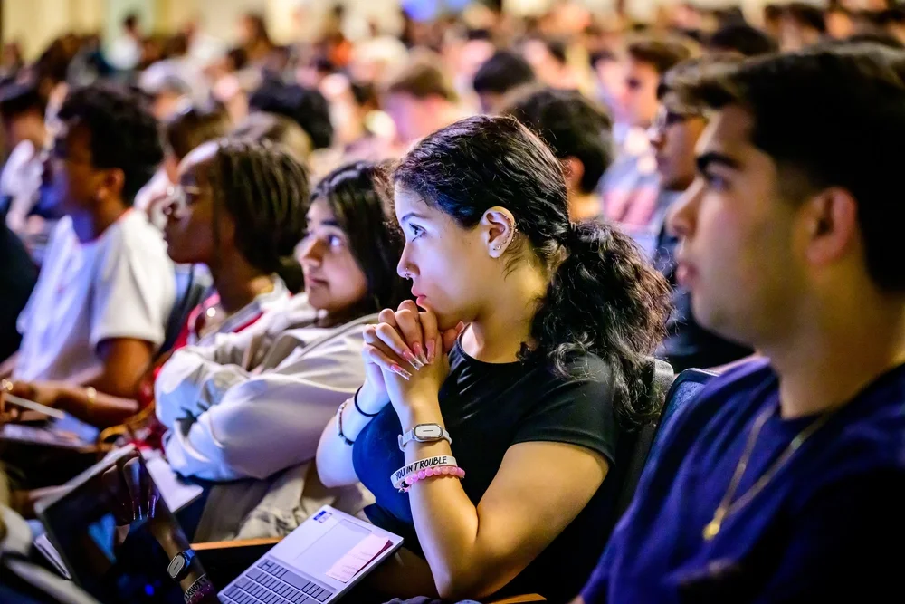 A student sitting in a lecture hall, listening to class.